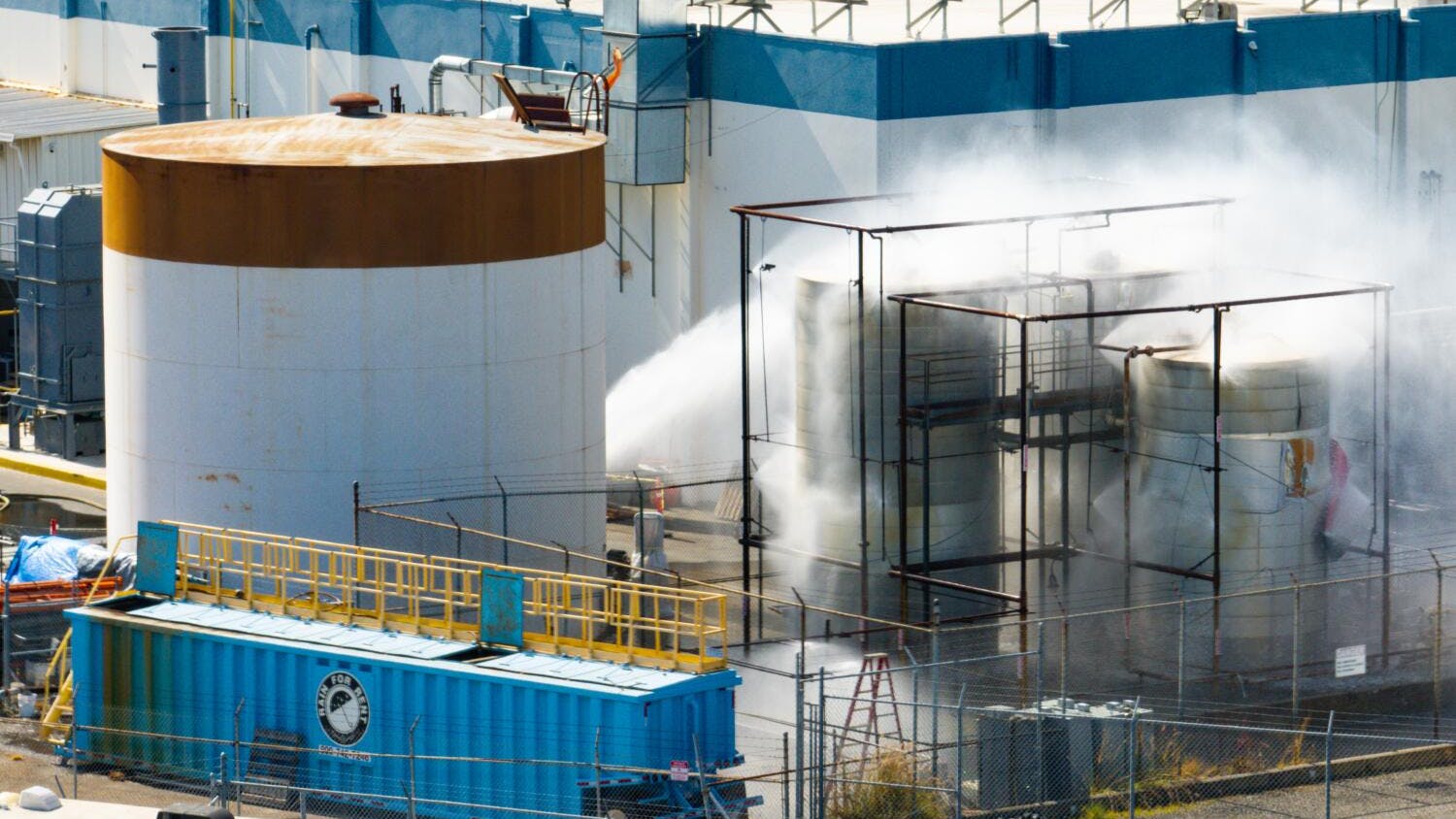 An aerial photograph of a large facility with water spraying onto one of the buildings