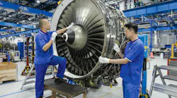 Two technicians wearing blue uniforms working on an airplane engine that's detached from a plane