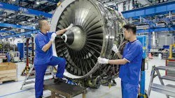 Two technicians wearing blue uniforms working on an airplane engine that's detached from a plane Two technicians wearing blue uniforms working on an airplane engine that's detached from a plane
