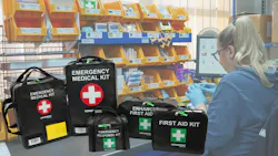 A woman wearing a blue hoodie and blue rubber gloves working next to a group of soft-case medical kits with labels like 'Emergency Medical Kit' and 'First Aid Kit' A woman wearing a blue hoodie and blue rubber gloves working next to a group of soft-case medical kits with labels like 'Emergency Medical Kit' and 'First Aid Kit'