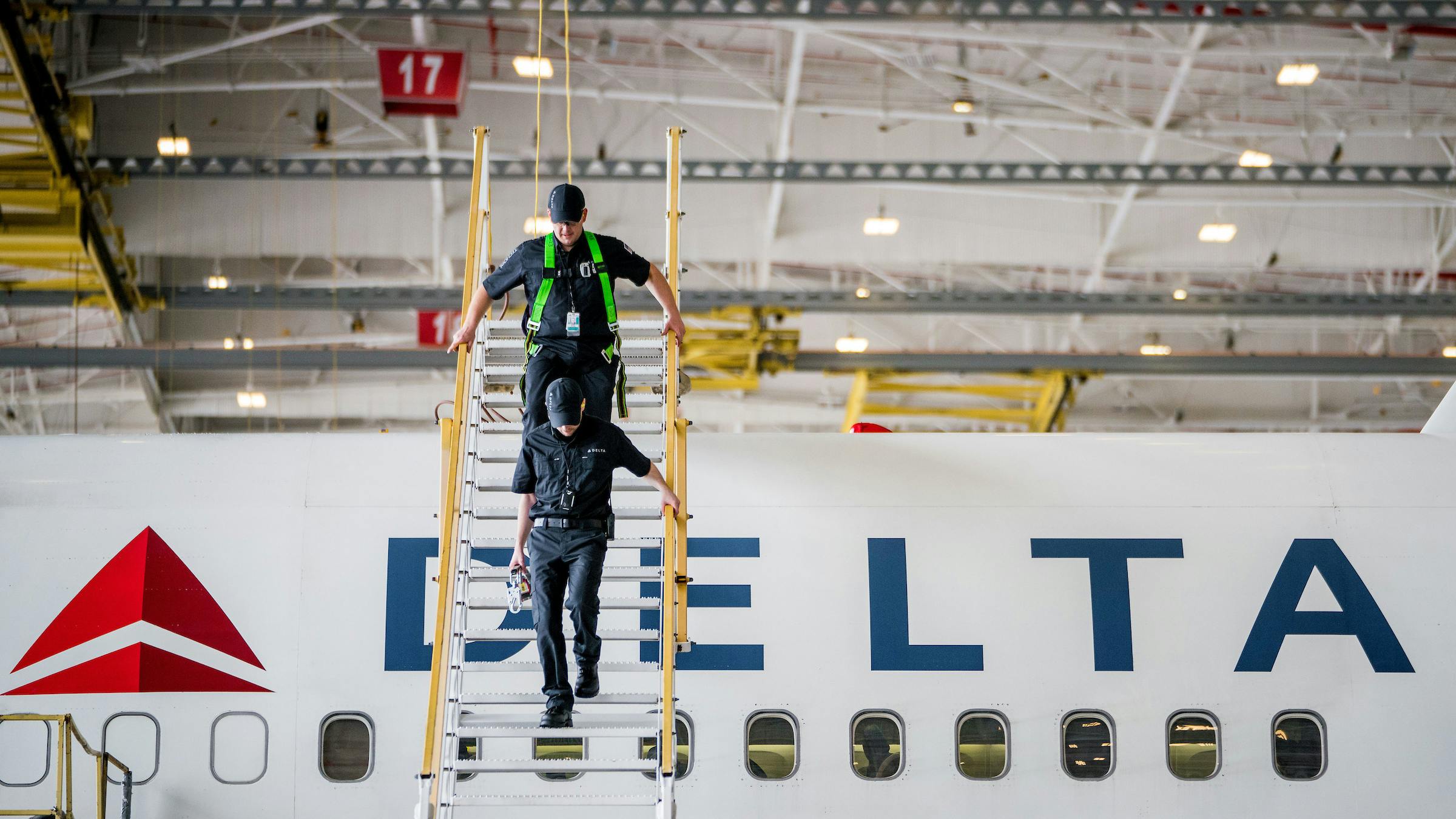 Two technicians climbing down a raised platform next to an airplane with text on the side that reads: DELTA