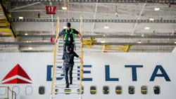 Two technicians climbing down a raised platform next to an airplane with text on the side that reads: DELTA Two technicians climbing down a raised platform next to an airplane with text on the side that reads: DELTA