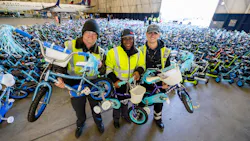 Three technicians wearing high-vis vests holding bicycles while standing in front of a room full of bicycles and scooters Three technicians wearing high-vis vests holding bicycles while standing in front of a room full of bicycles and scooters