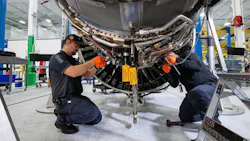 Two technicians wearing dark blue uniforms working underneath an airplane engine Two technicians wearing dark blue uniforms working underneath an airplane engine