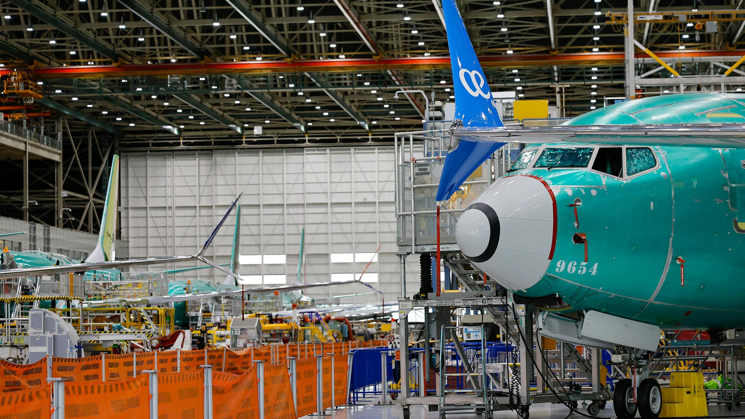 A wide shot of an aircraft production warehouse, with airplanes lined up among machinery