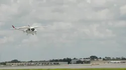 A white aircraft flying above an airport runway
