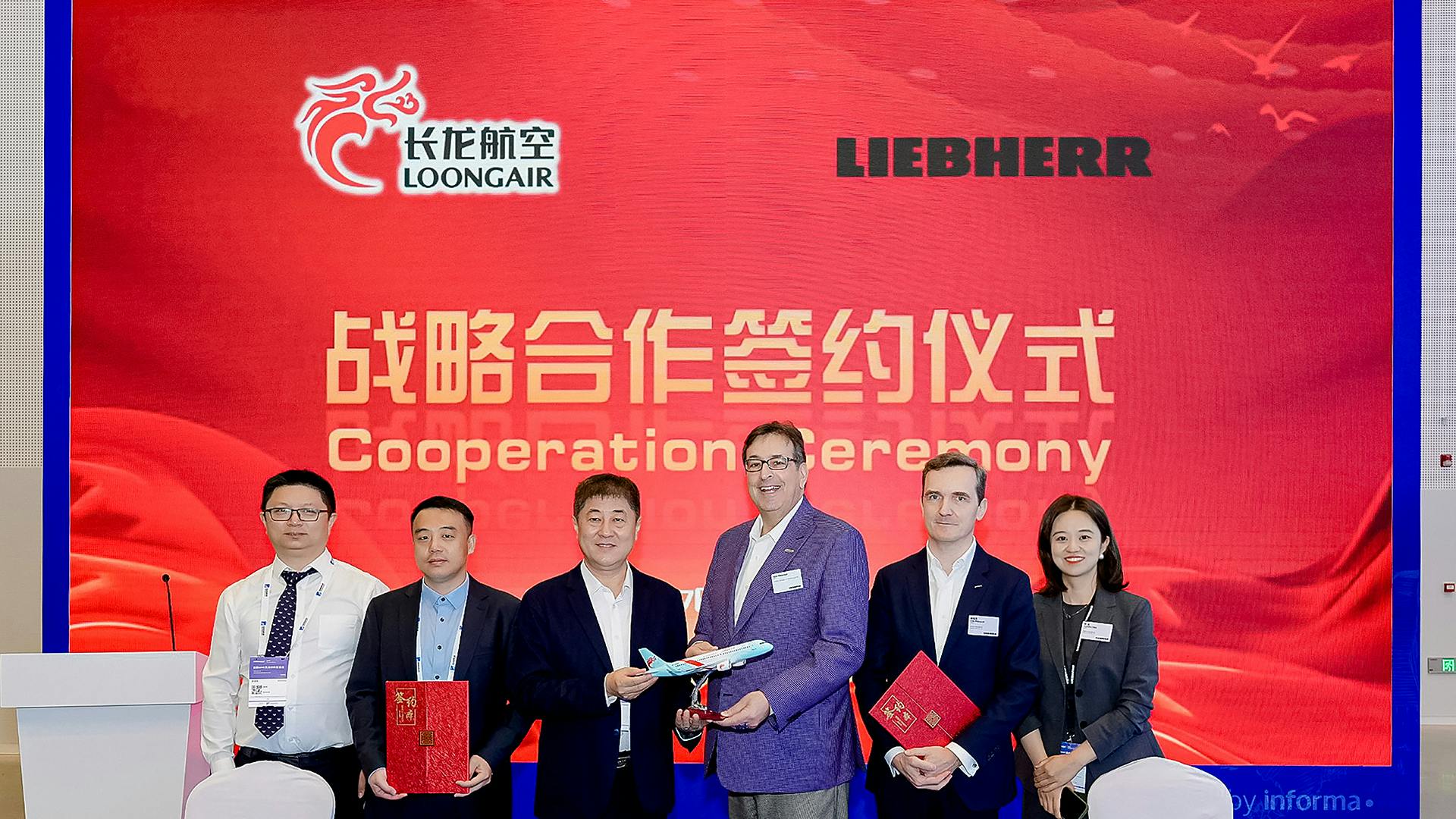 A line of people wearing business attire standing behind a table and holding paperwork while smiling at the camera in front of a backdrop that reads: Cooperation Ceremony Loong Air Liebherr