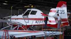A red and white seaplane parked on a platform while a man checks a rear compartment