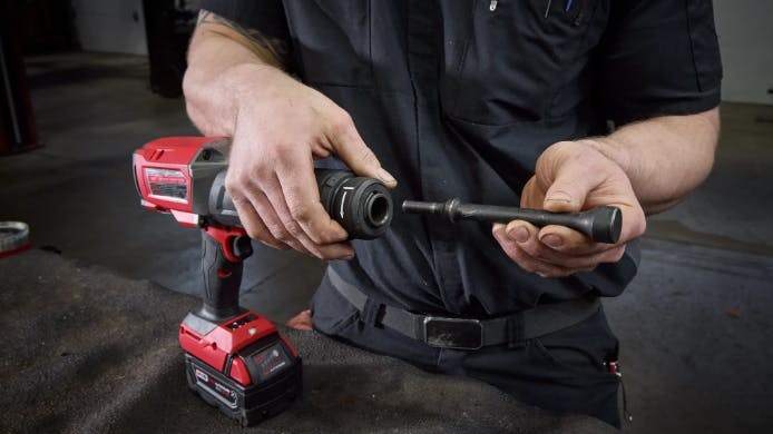 A person holding a large hammer chisel tool, holding the bit separate from the base, which is red and black