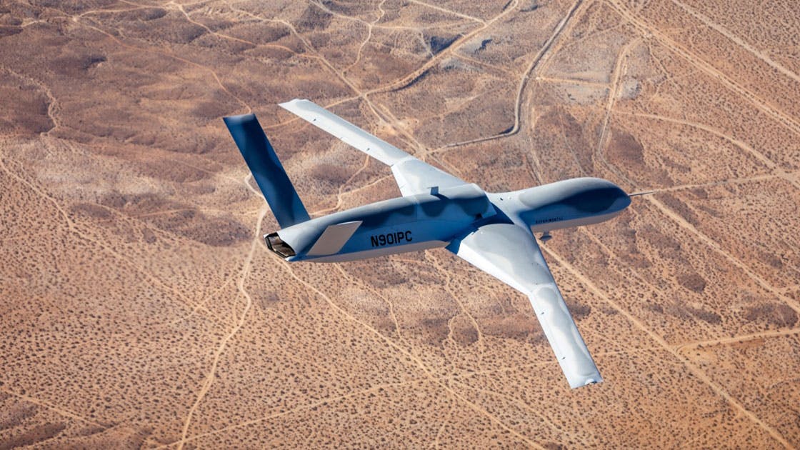 A gray airplane flying over desert landscape