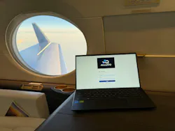 A laptop perched on someone's lap displaying a homepage with text that says. 'AircraftIQ' while seated on an airplane in the air, the window in the background A laptop perched on someone's lap displaying a homepage with text that says. 'AircraftIQ' while seated on an airplane in the air, the window in the background