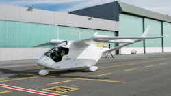 A small white aircraft with a person in the cockpit landing on a black runway at an airport A small white aircraft with a person in the cockpit landing on a black runway at an airport