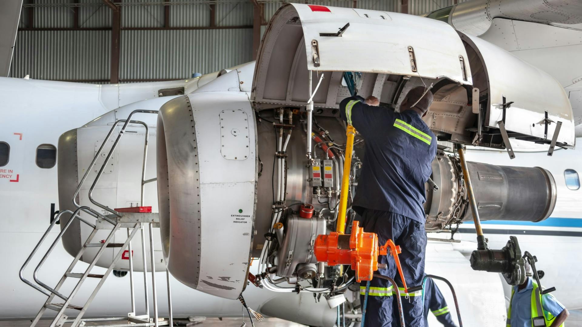 A technician wearing a dark blue uniform working on an airplane engine that's opened up