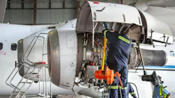 A technician wearing a dark blue uniform working on an airplane engine that's opened up A technician wearing a dark blue uniform working on an airplane engine that's opened up