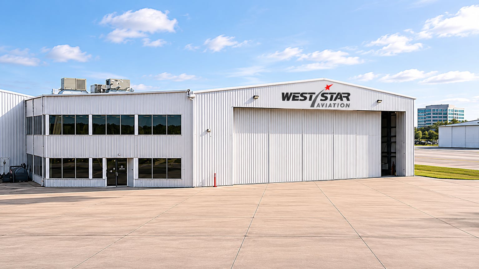 An outdoor shot of a warehouse-type facility with a sign that reads: West Star Aviation underneath a blue sky with clouds