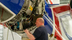 A man wearing a dark blue polo shirt standing next to an opened airplane engine and looking inside