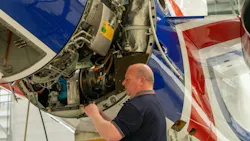 A man wearing a dark blue polo shirt standing next to an opened airplane engine and looking inside A man wearing a dark blue polo shirt standing next to an opened airplane engine and looking inside