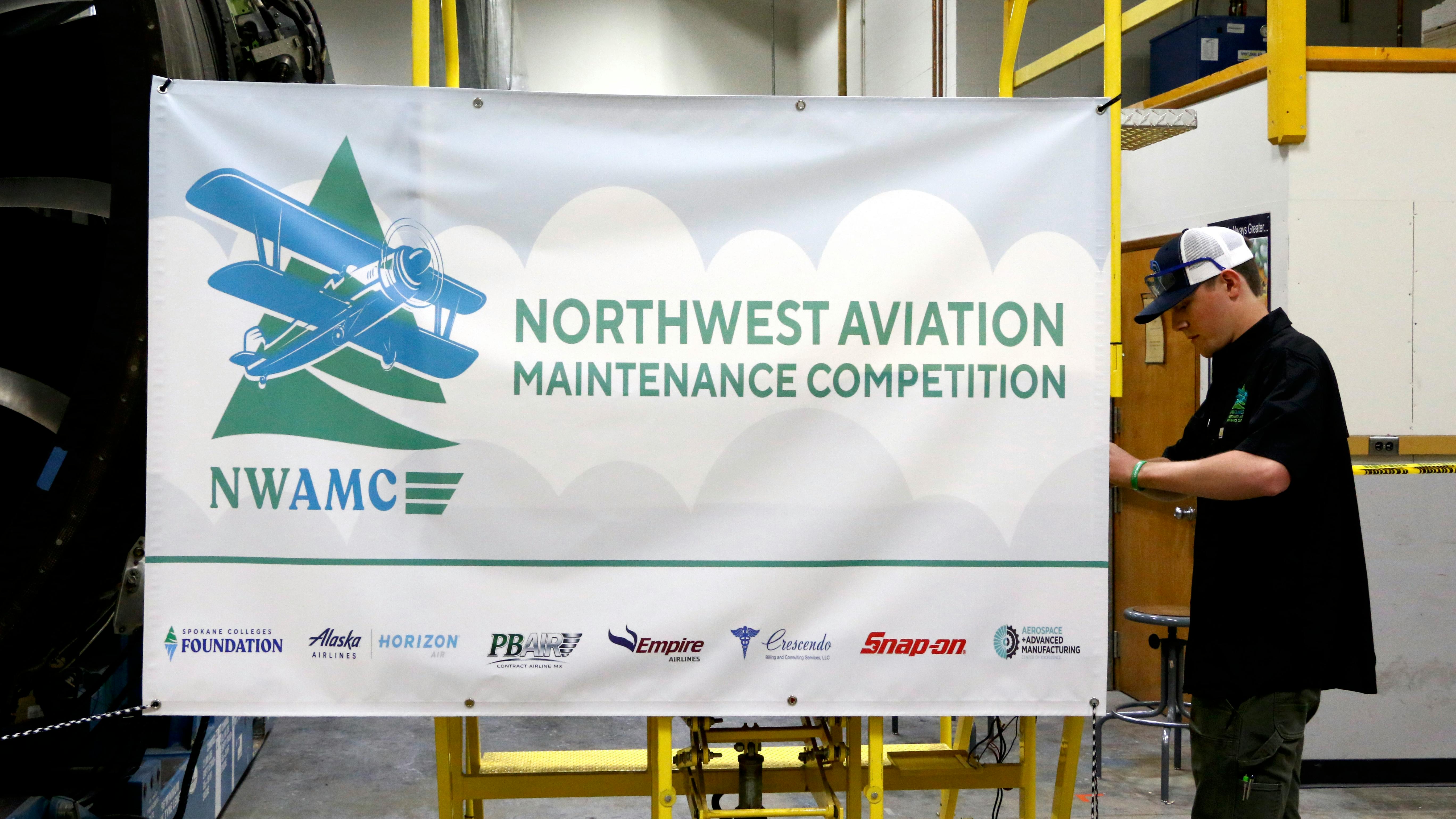 A young man putting up a banner that reads: NWAMC Northwest Aviation Maintenance Competition