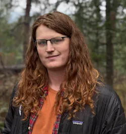 A man with long brown hair standing outside and smiling at the camera A man with long brown hair standing outside and smiling at the camera