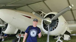 A young man giving a thumbs-up and smiling at the camera, standing in front of a white airplane parked in grass A young man giving a thumbs-up and smiling at the camera, standing in front of a white airplane parked in grass