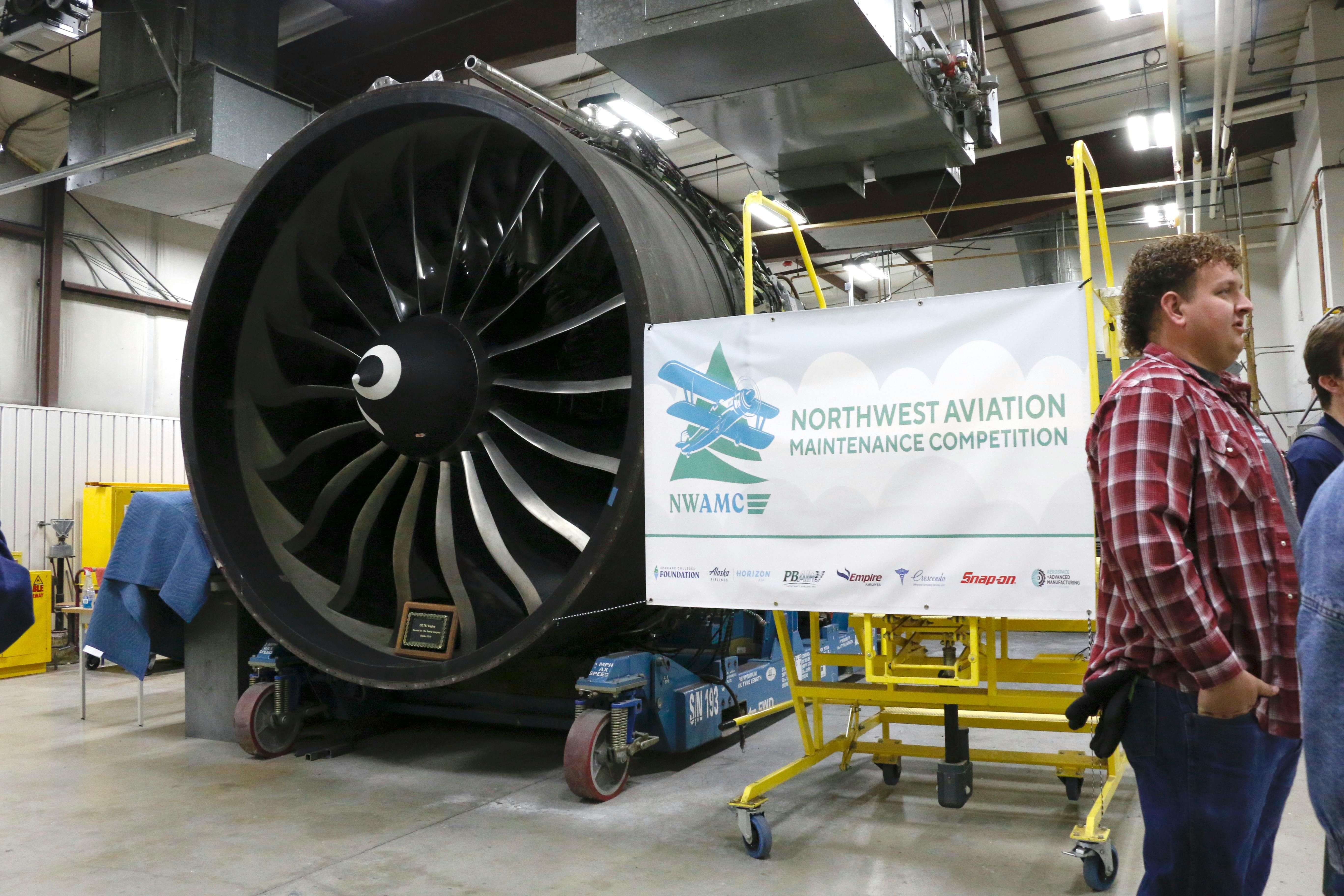 An airplane engine next to a banner that reads: NWAMC Northwest Aviation Maintenance Competition