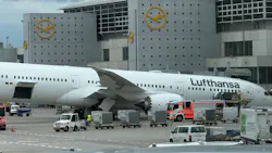 An airplane on the ground with ground handling equipment driving around it, with the word 'Lufthansa' printed on the plane An airplane on the ground with ground handling equipment driving around it, with the word 'Lufthansa' printed on the plane