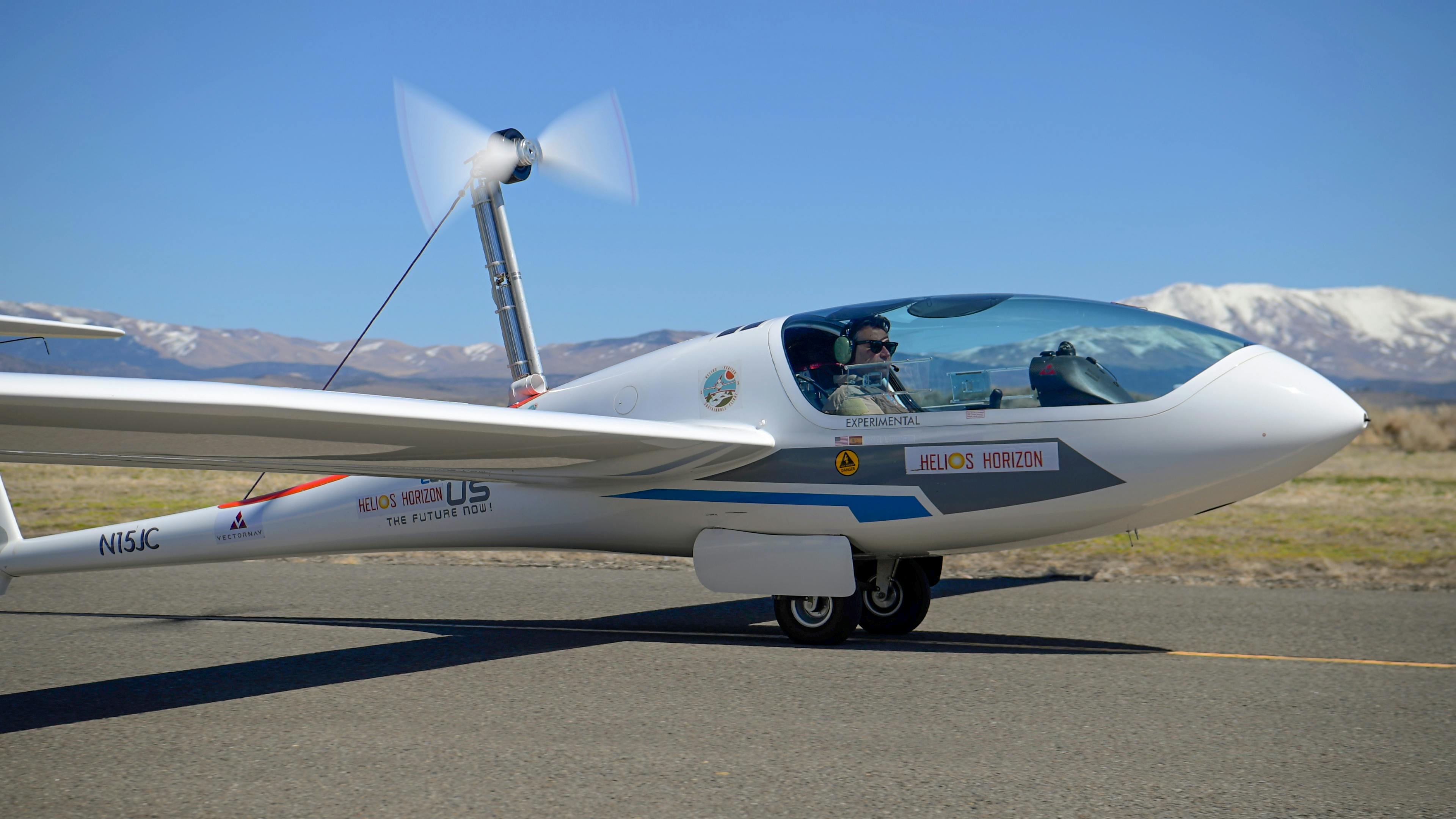 A small electric aircraft with a pilot in the cockpit landing on a runway