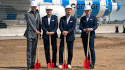 Four men wearing suits and white hard hats holding shovels that are pointed into the ground on a worksite Four men wearing suits and white hard hats holding shovels that are pointed into the ground on a worksite