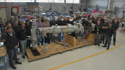 A large group of people gathered around a piece of aircraft landing gear in a repair shop A large group of people gathered around a piece of aircraft landing gear in a repair shop