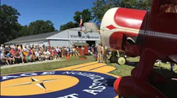 A close-up image of a red vintage airplane with a crowd in the background