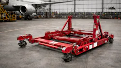 A red engine stand sitting on the floor of a repair shop with an airplane in the background A red engine stand sitting on the floor of a repair shop with an airplane in the background