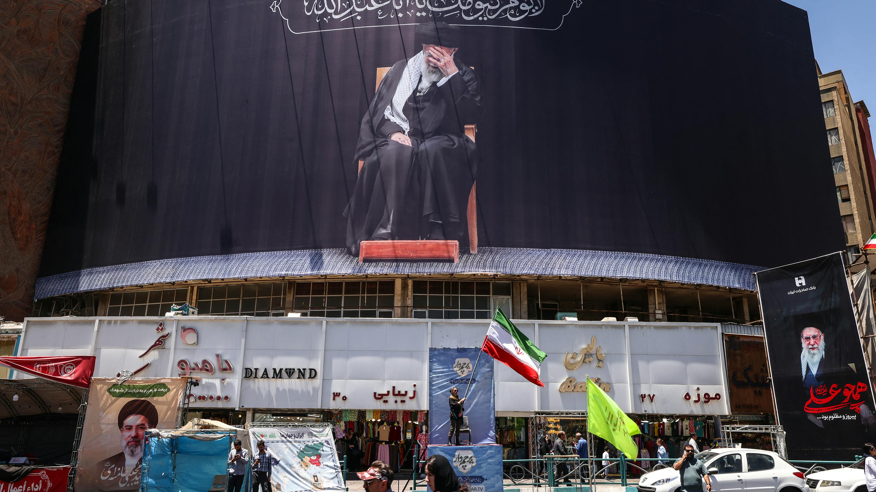 An Iranian woman waves a national flag under a billboard depicting slain supreme leader Ayatollah Ali Khamenei at Valiasr Square in Tehran on June 15, 2026. The United States and Iran agreed a peace deal and an 'immediate and permanent' end to military operations on all fronts including Lebanon, mediator Pakistan said, signaling the apparent end to more than three months of war in Middle East.