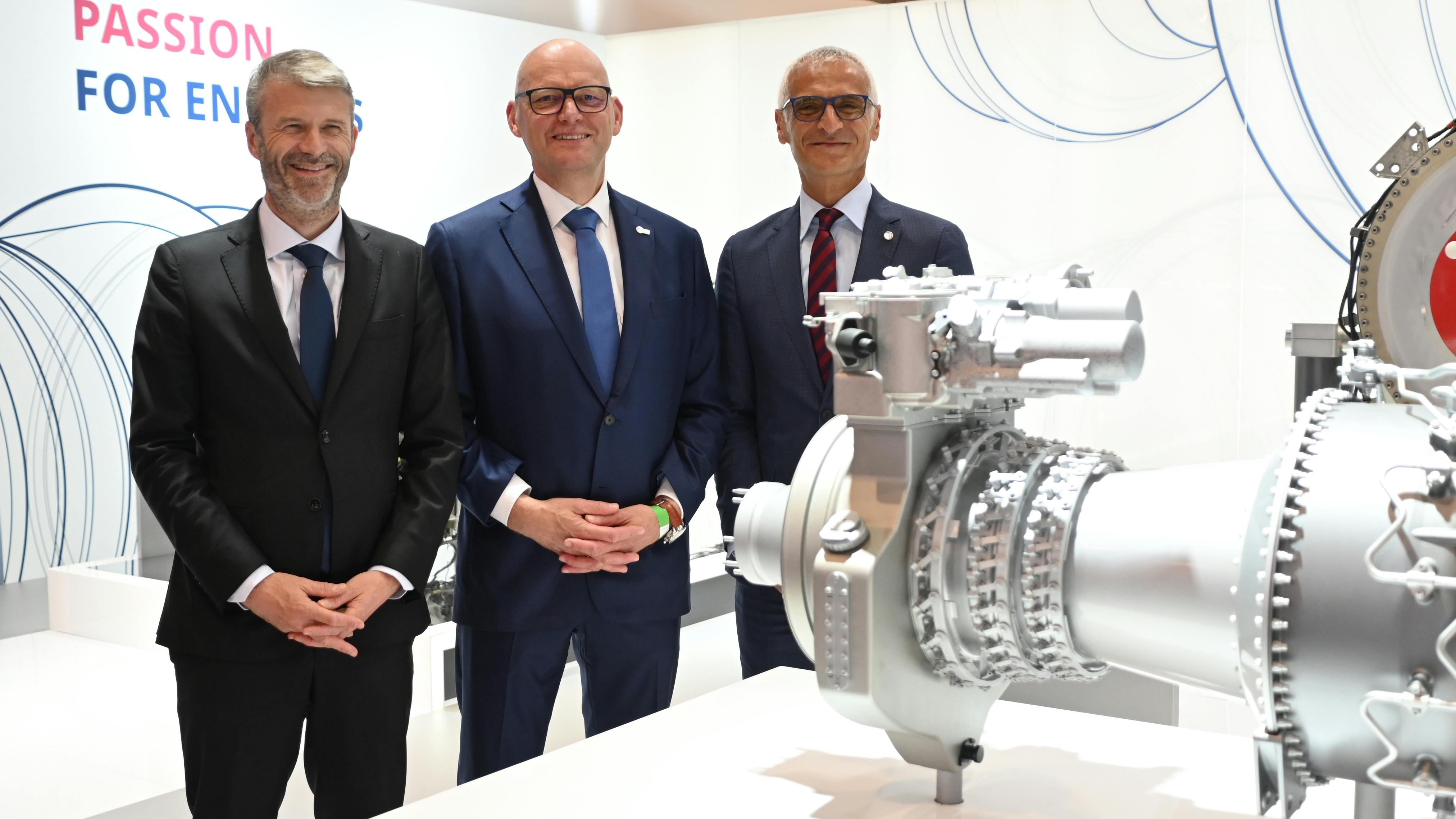 Three men wearing suits smiling at the camera and standing next to an airplane engine