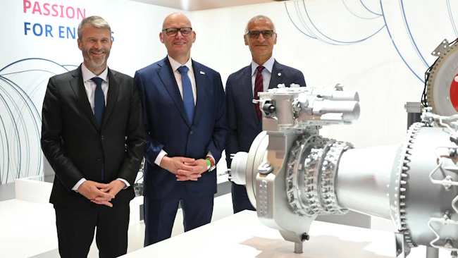 Three men wearing suits smiling at the camera and standing next to an airplane engine