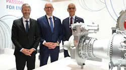 Three men wearing suits smiling at the camera and standing next to an airplane engine