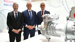 Three men wearing suits smiling at the camera and standing next to an airplane engine Three men wearing suits smiling at the camera and standing next to an airplane engine