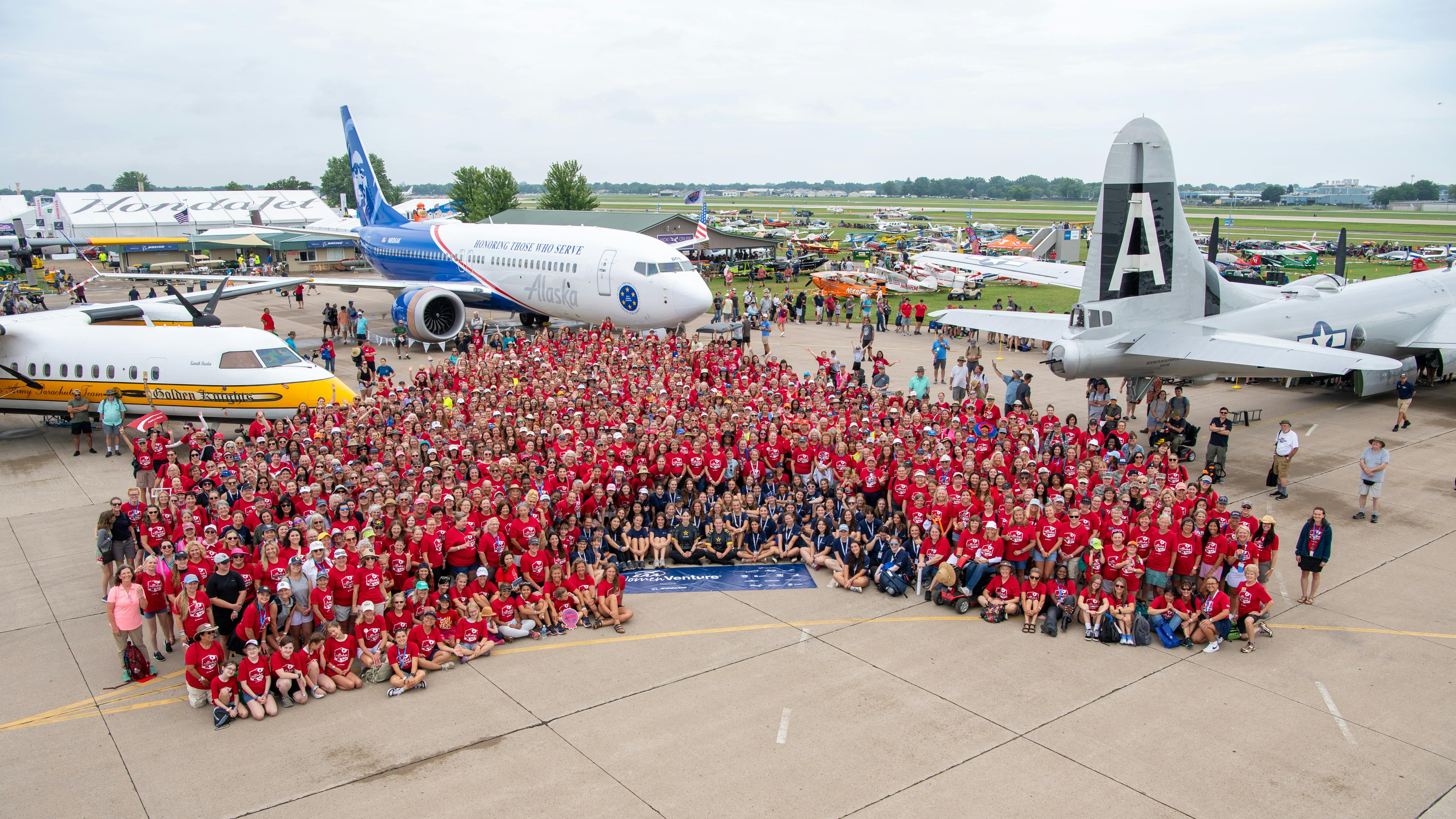 A huge crowd of people wearing red shirts and standing in front of a collection of airplanes