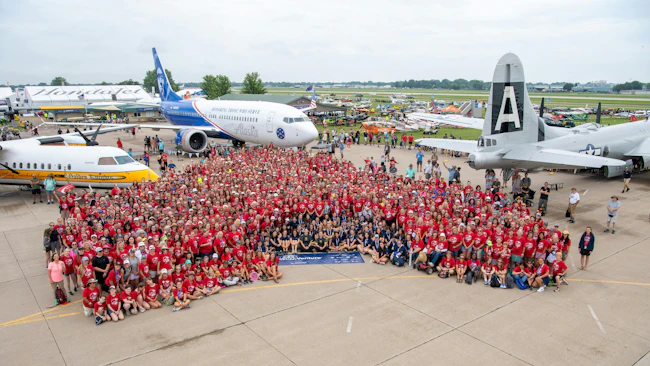 A huge crowd of people wearing red shirts and standing in front of a collection of airplanes