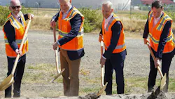 Four men wearing business attire and bright orange vests digging shovels into a pile of dirt Four men wearing business attire and bright orange vests digging shovels into a pile of dirt