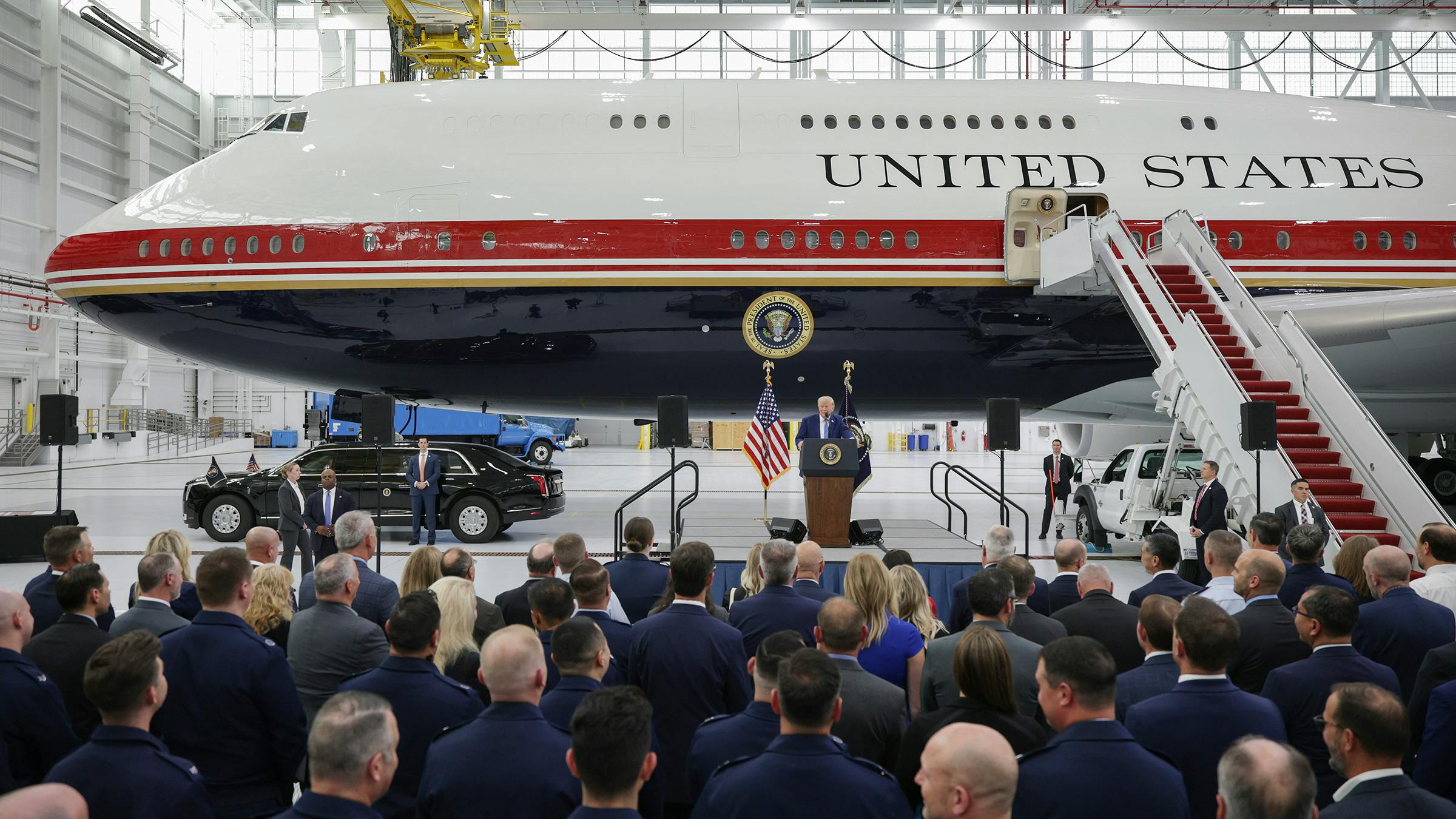 A group of people watching a speaker in front of a large airplane with text printed on it that reads: UNITED STATES