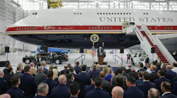 A group of people watching a speaker in front of a large airplane with text printed on it that reads: UNITED STATES