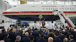 A group of people watching a speaker in front of a large airplane with text printed on it that reads: UNITED STATES A group of people watching a speaker in front of a large airplane with text printed on it that reads: UNITED STATES