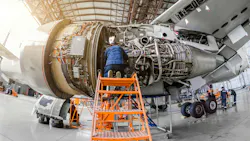 A technician at the top of an orange work platform with stairs, working on an opened-up airp[ane engine A technician at the top of an orange work platform with stairs, working on an opened-up airp[ane engine