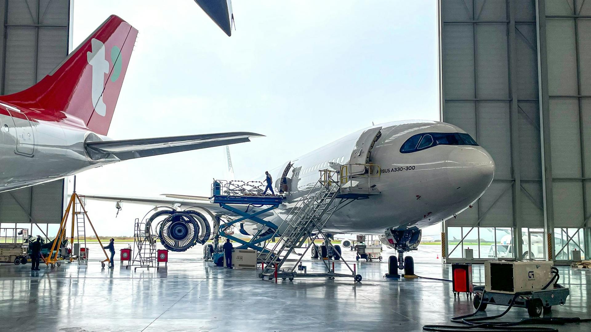 An airplane parked halfway inside a maintenance hangar, with a technician walking out the door