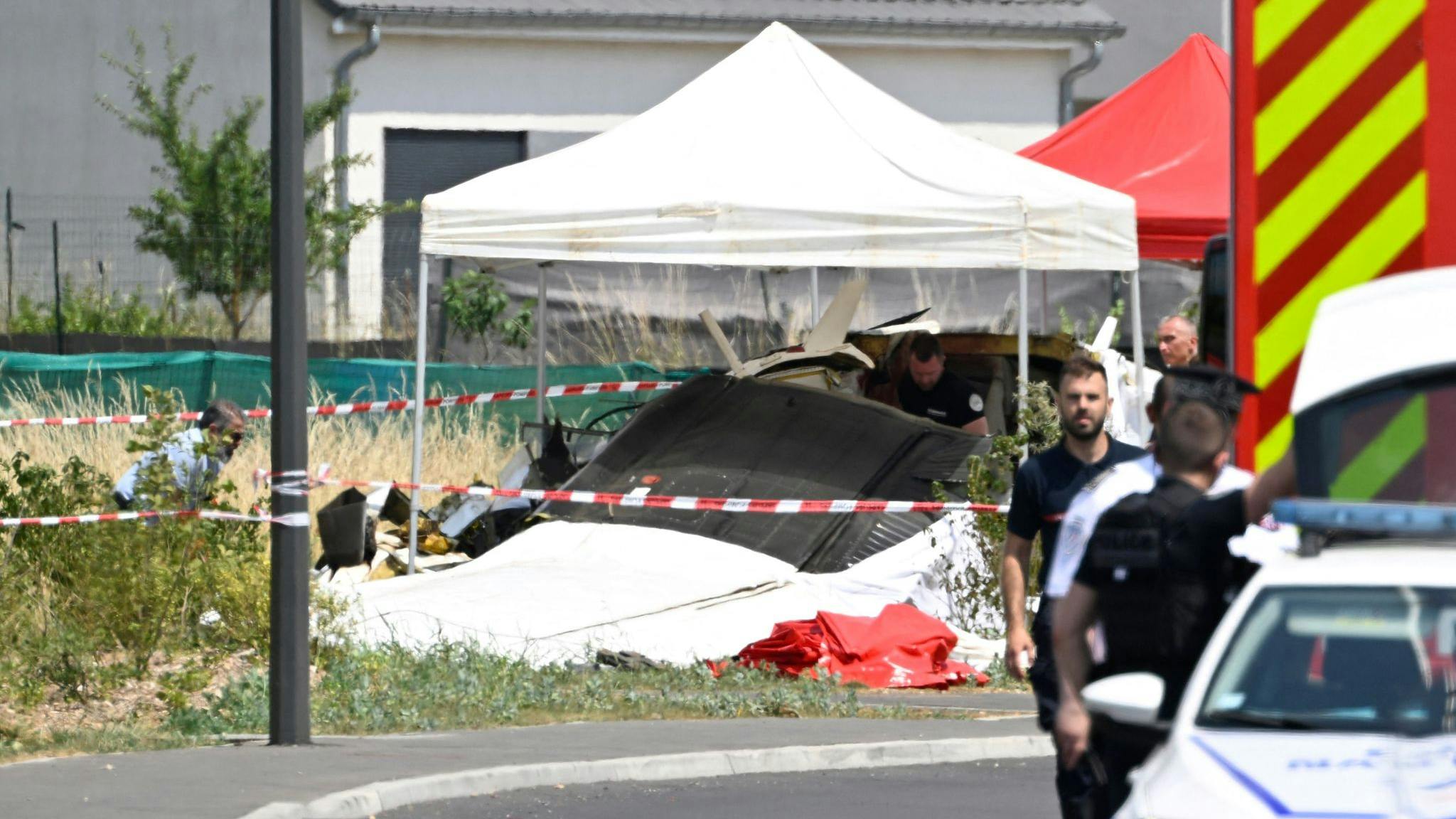 A white tent set up over the remnants of a plane crash, with a police officer standing in the foreground