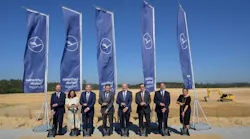 A group of professionals wearing business attire standing at a construction site, digging shovels into the ground