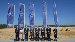 A group of professionals wearing business attire standing at a construction site, digging shovels into the ground