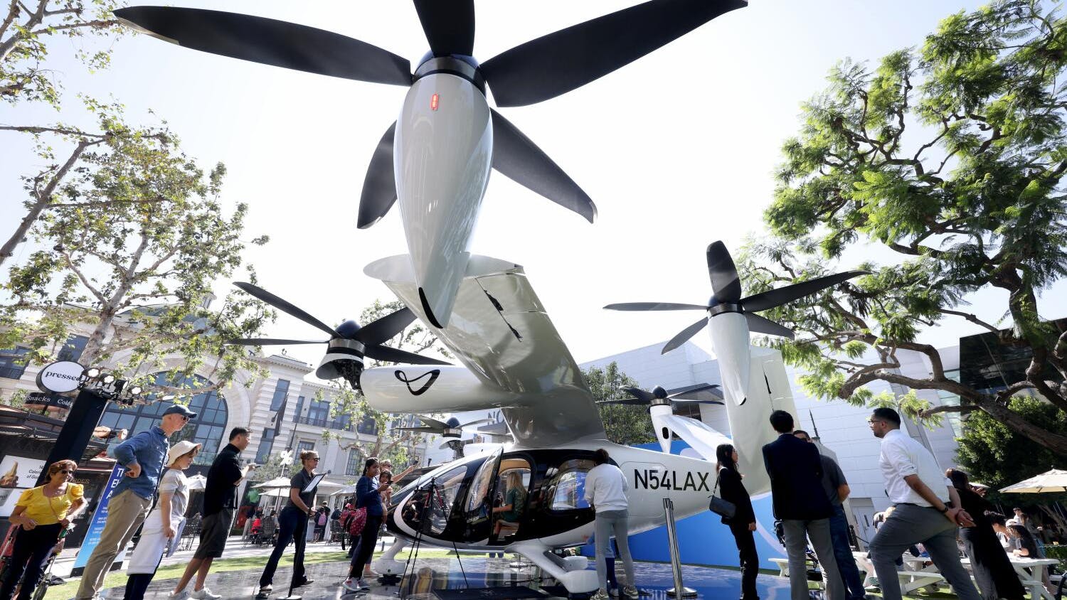 A group of people standing under a large electric aircraft with four propellers
