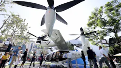 A group of people standing under a large electric aircraft with four propellers