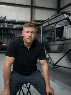A man wearing a black polo looking seriously at the camera while crouching